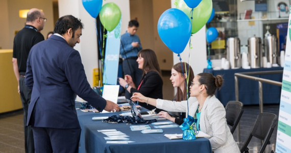 man in suit checking in at registration table with navy linens, balloons and three women seated